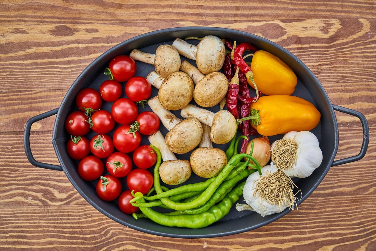 A casserole dish filled with various raw ingredients including tomatoes, mushrooms, peppers, and garlic