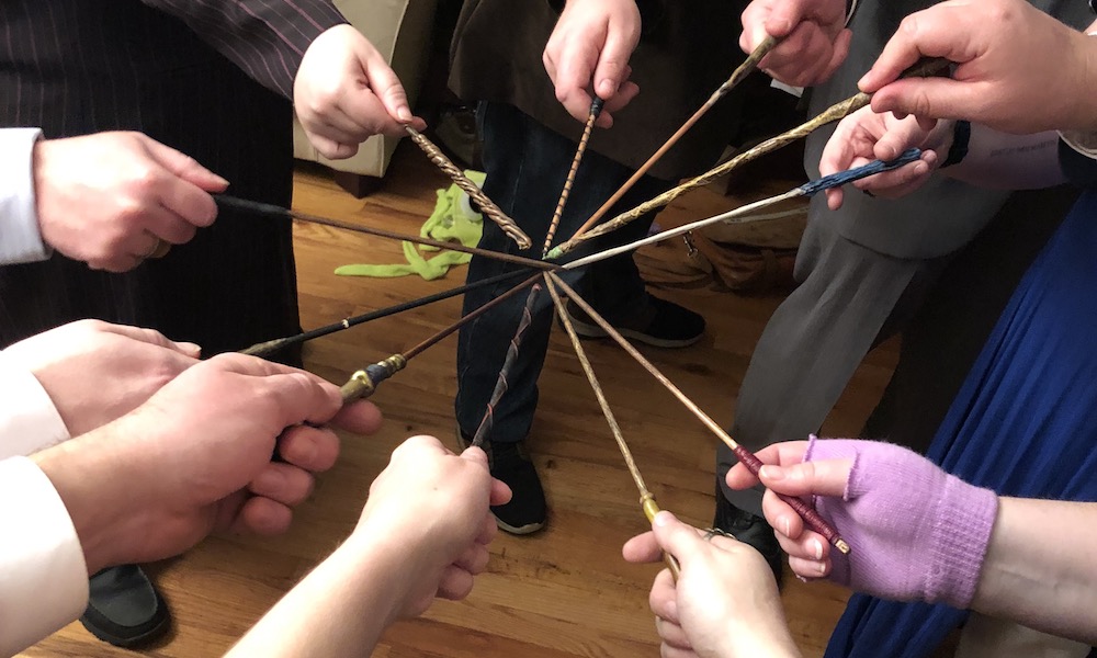 11 hands all pointing various harry potter-esque wands in to the center