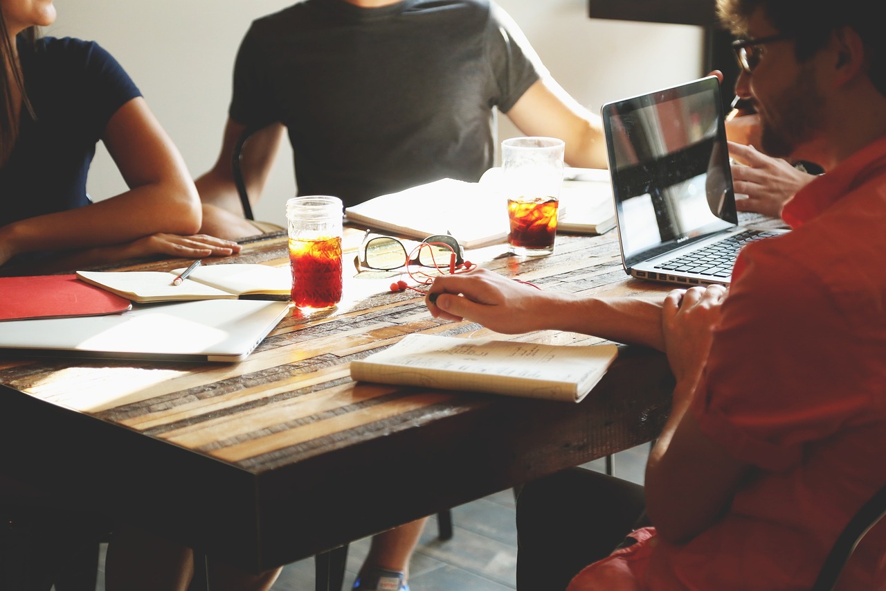 Four people sitting around a table with some notebooks, beverages, and a laptop.