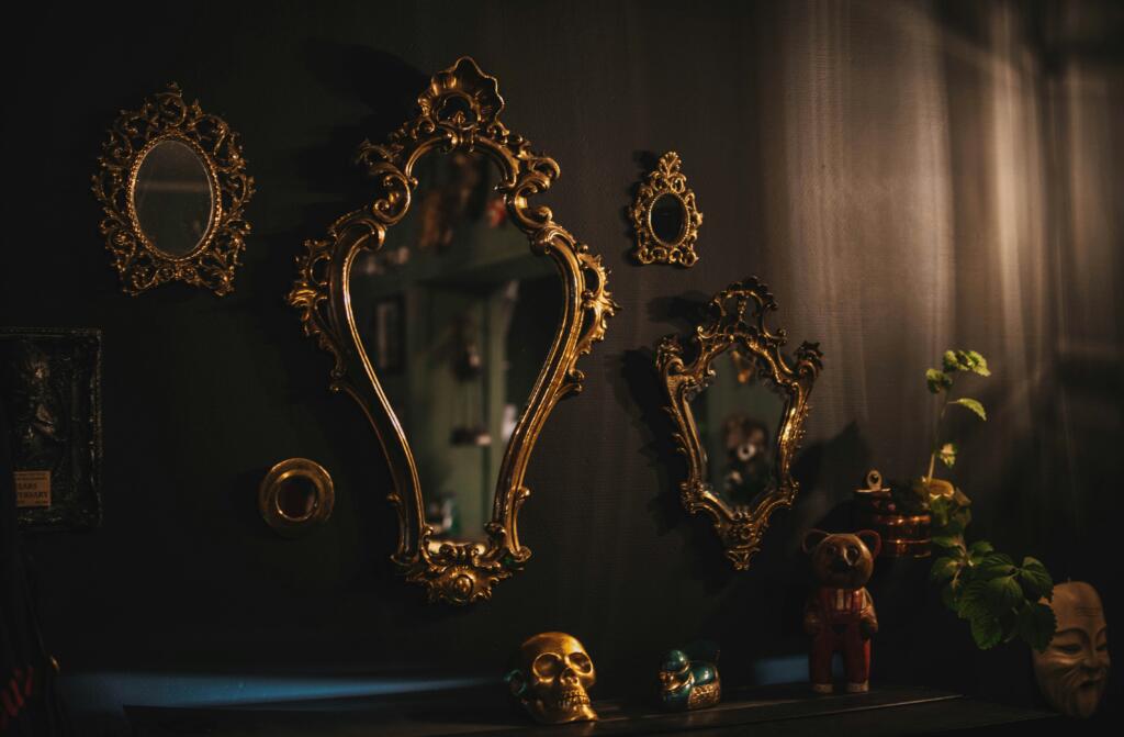 A series of antique mirrors in gold frames hung on a dark wall above a row of knickknacks sitting on a sideboard.